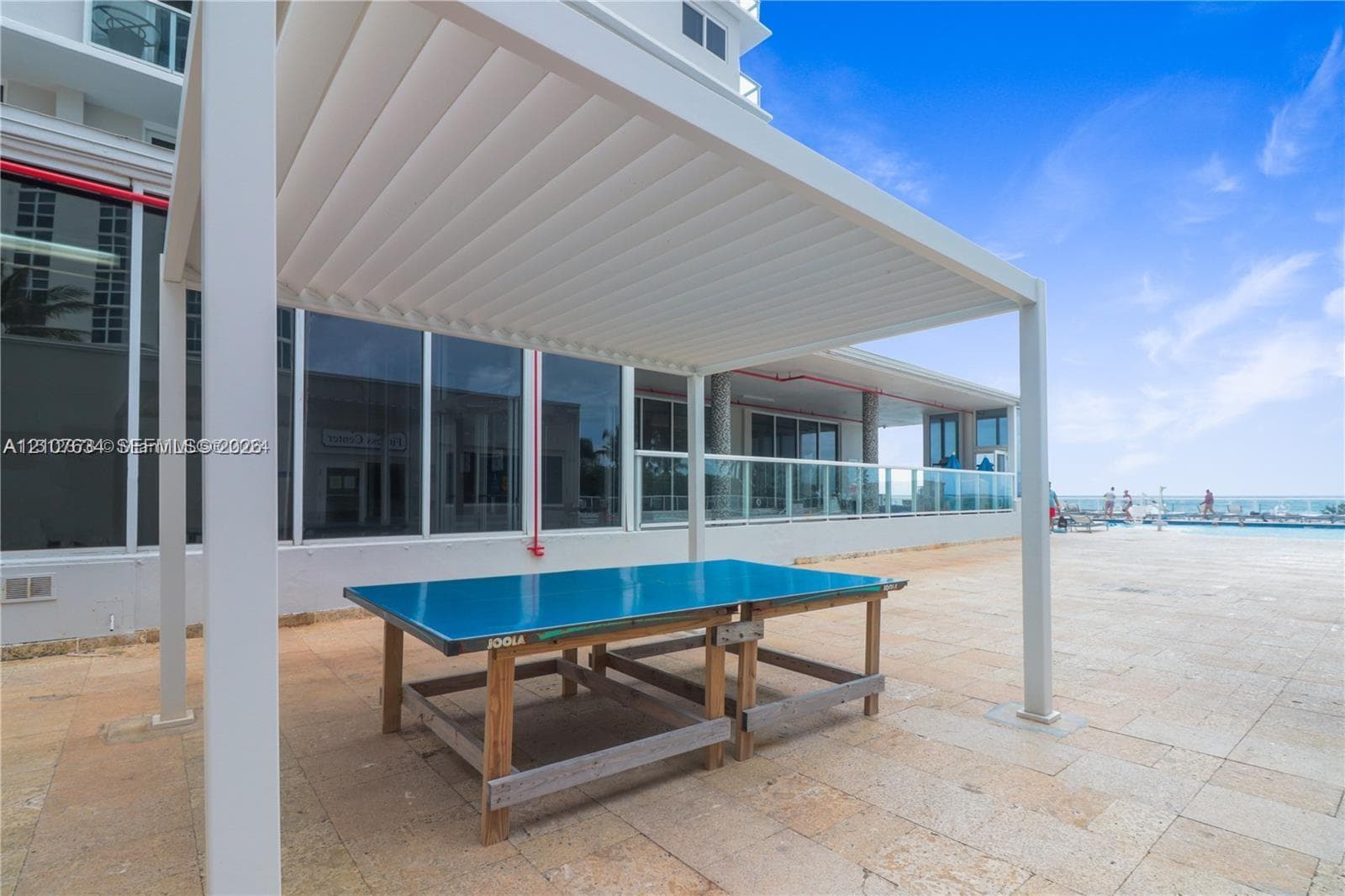 Outdoor terrace featuring a louvered pergola, stone-tile flooring, and a glass-paneled railing