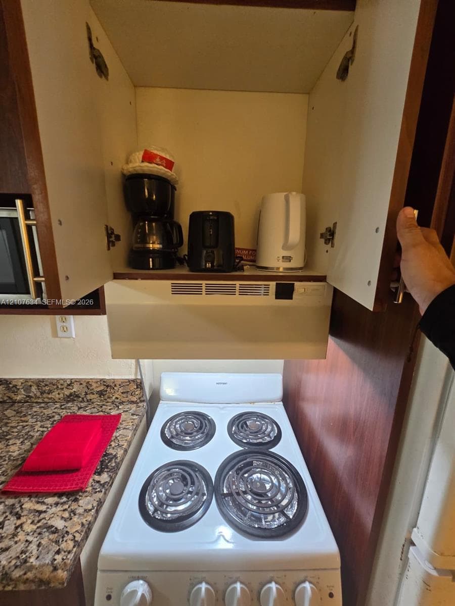 White four-burner electric range with integrated hood ventilation and natural stone-finish countertops