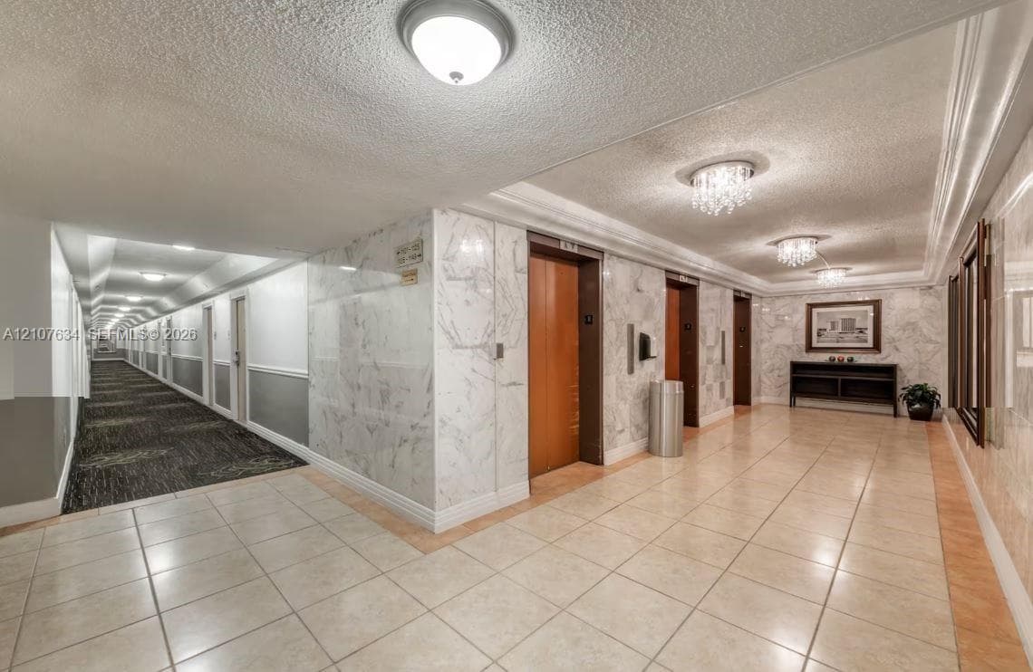 Common area lobby featuring natural stone wall cladding, polished tile flooring, multiple elevator banks with wood-finish doors, and decorative crystal-style ceiling flush-mount lighting