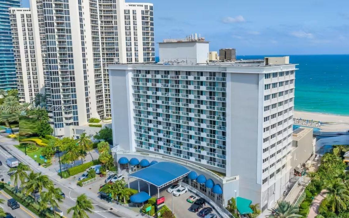 High-rise coastal building featuring a prominent covered porte-cochère, balcony-lined exterior facade, and direct proximity to the oceanfront