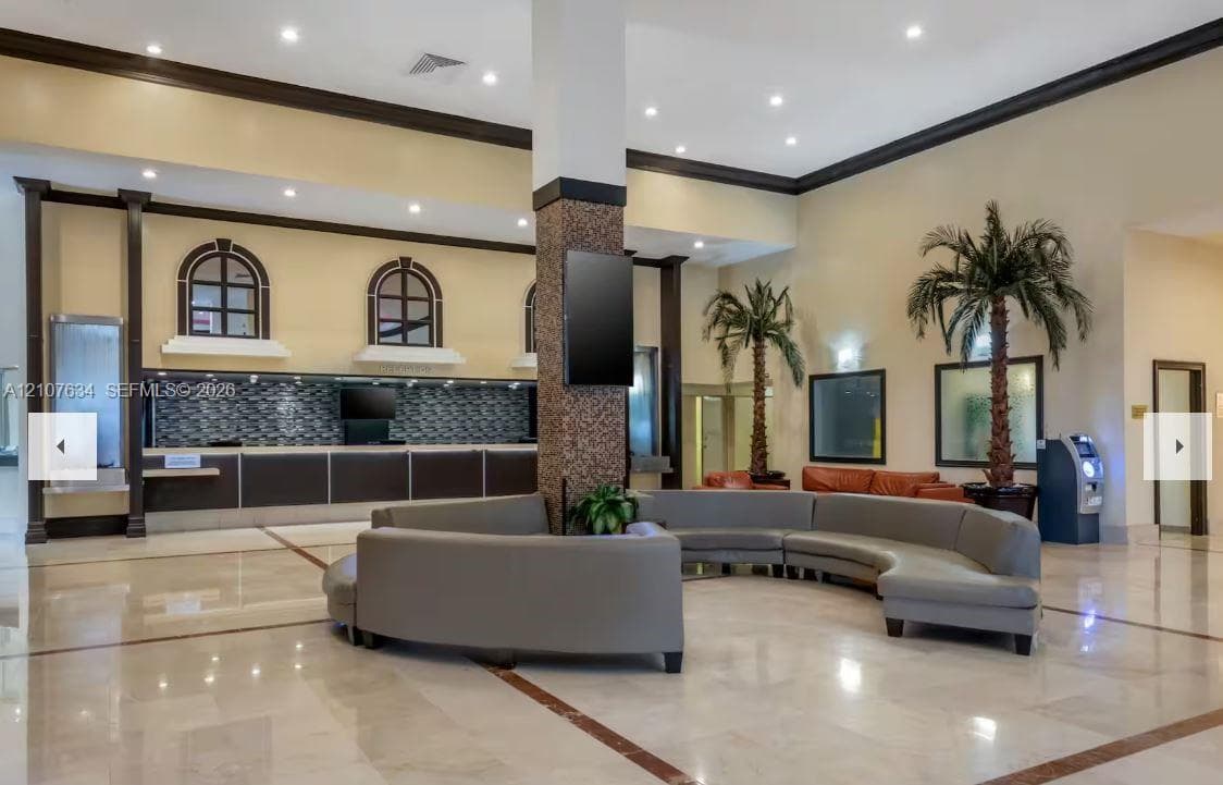 Grand lobby featuring stone-tile flooring, vaulted ceilings with recessed lighting, custom built-in service counter with decorative tile backsplash, and architectural crown molding