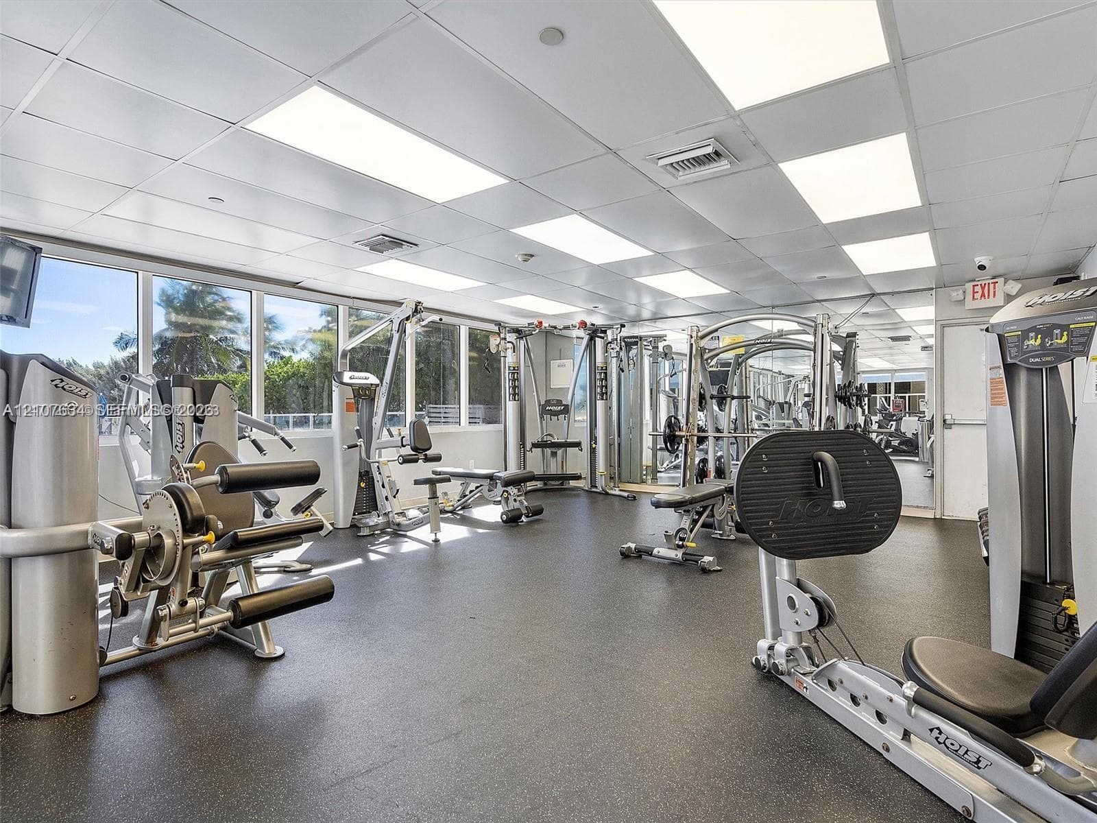 Fitness center featuring floor-to-ceiling windows, rubberized flooring, mirrored walls, and grid ceiling panels with recessed lighting