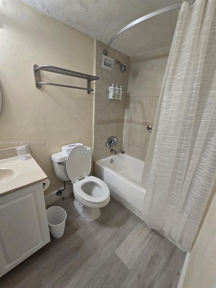 Bathroom featuring wood-finish flooring, a white cabinet vanity, a shower-tub combination with tiled surround, and a metal wall-mounted towel rack
