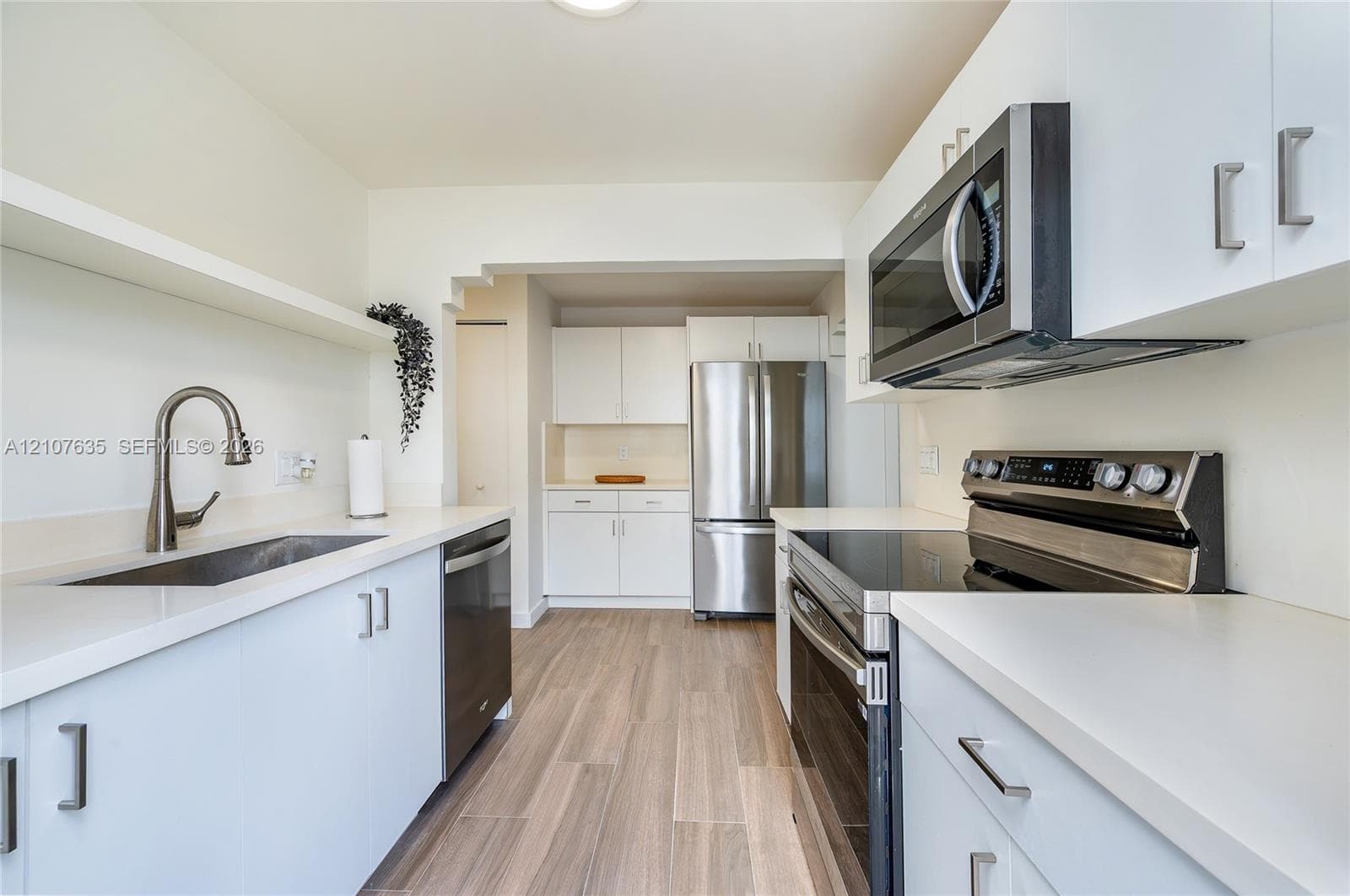 Kitchen featuring white flat-panel cabinetry, light-toned solid surface countertops, stainless steel appliances, a high-arc pull-down faucet, and wood-finish flooring