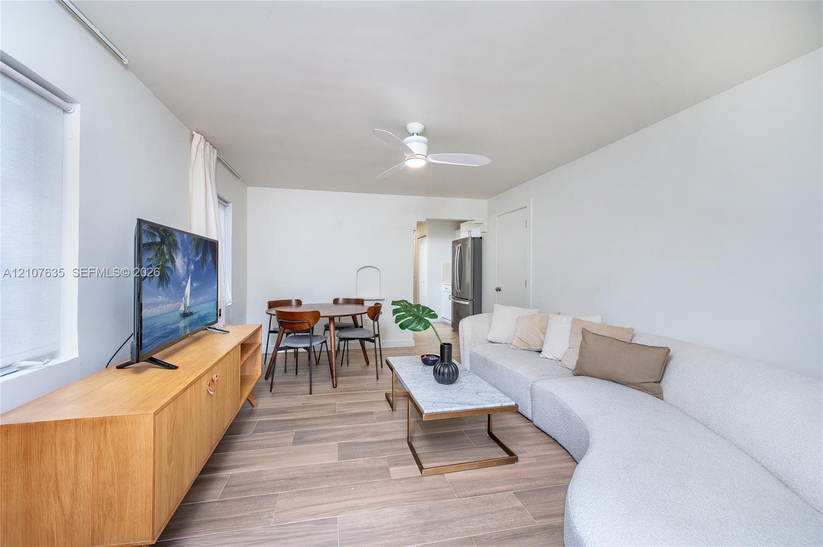 Living space featuring wood-finish flooring, white walls, and a ceiling-mounted light fixture with fan