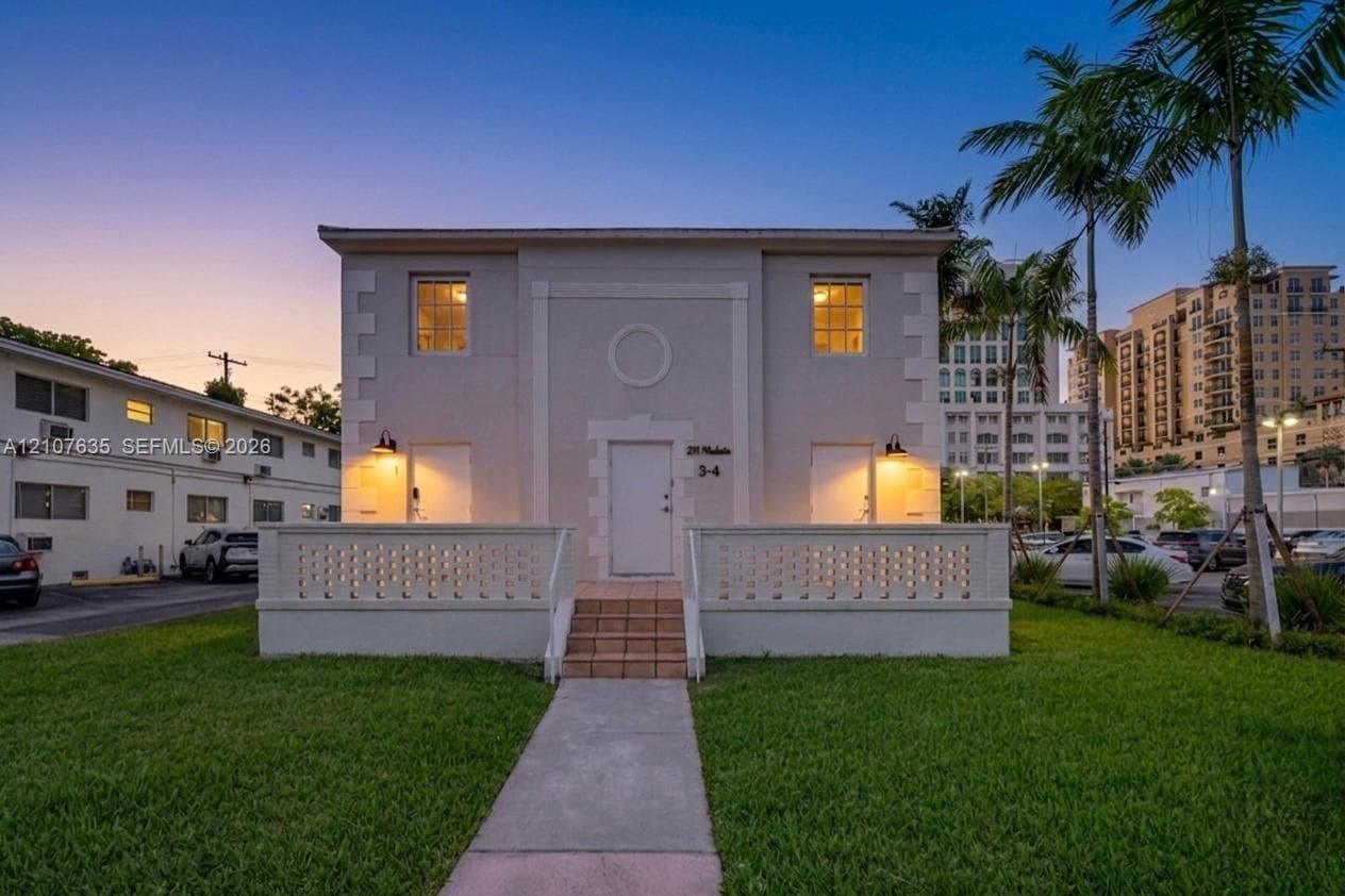 Two-story exterior featuring light-toned masonry, a decorative breeze block railing, exterior sconce lighting, and a central tiled stairway