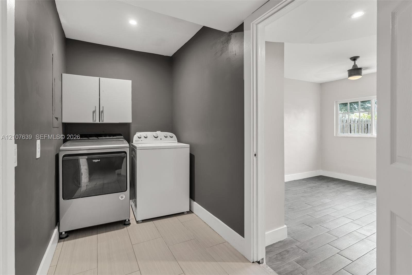 Laundry area featuring neutral-toned tile flooring, charcoal-painted walls, and white upper cabinetry