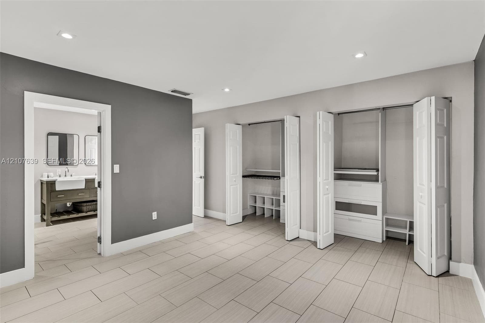 Ceramic tile flooring, recessed lighting, dual closets with interior built-in shelving, and entry to bathroom featuring a wooden vanity with undermount sink