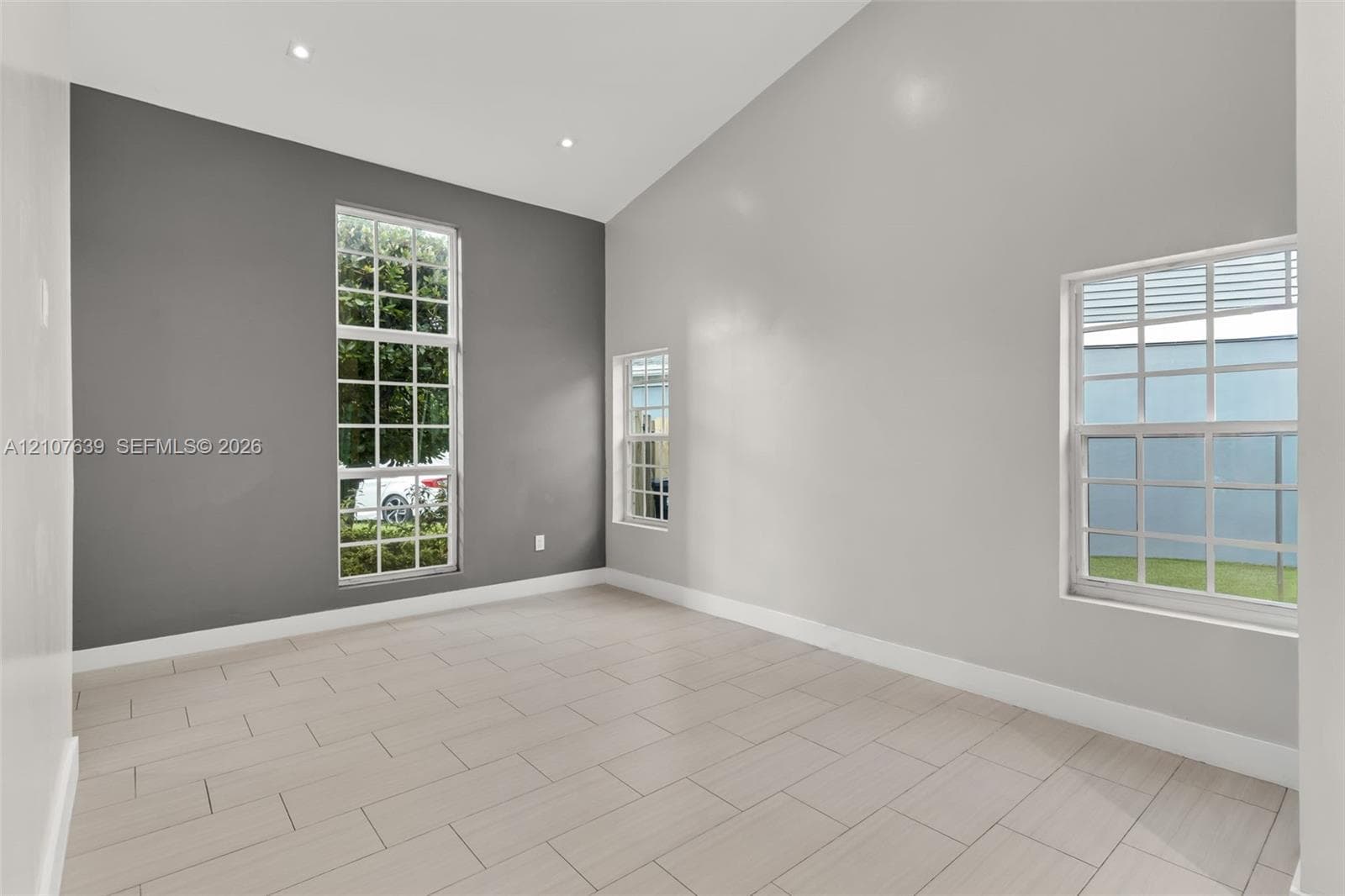 Vaulted ceilings featuring recessed lighting, large grid-pattern windows, and neutral-tone tile flooring