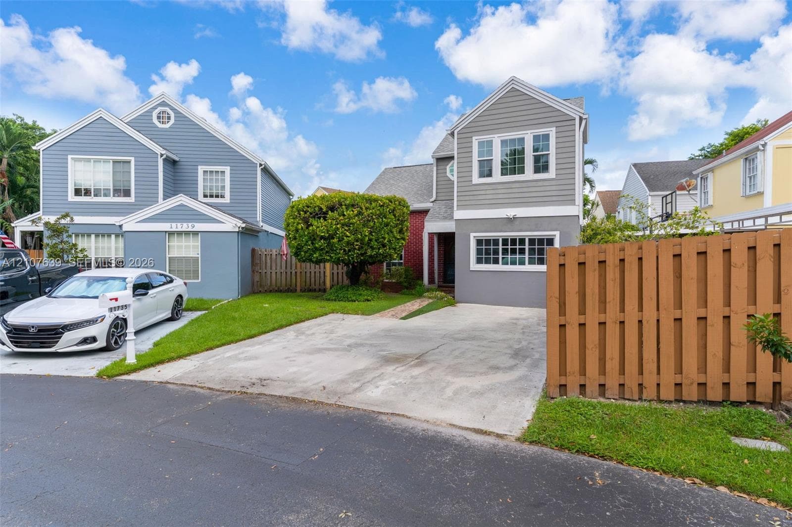 Two-story exterior featuring grey horizontal siding, multi-pane windows, a concrete driveway, and a wood-slat privacy fence