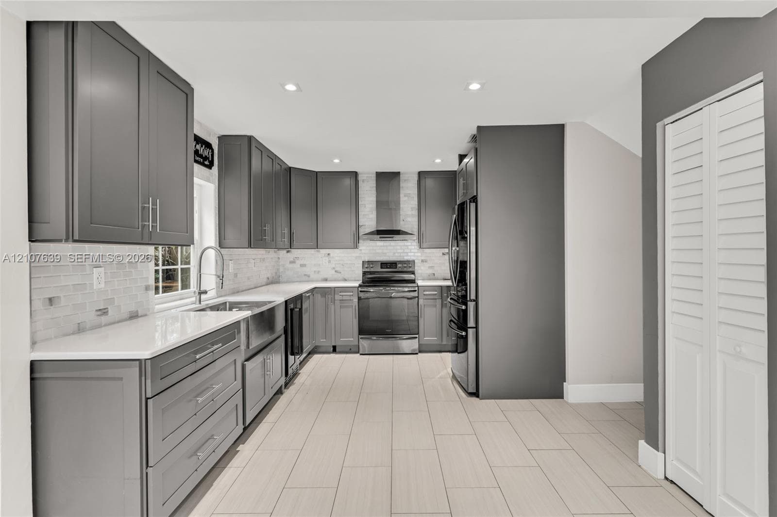 Kitchen featuring dark grey shaker-style cabinetry, quartz countertops, white subway tile backsplash, stainless steel appliances, and rectified tile flooring