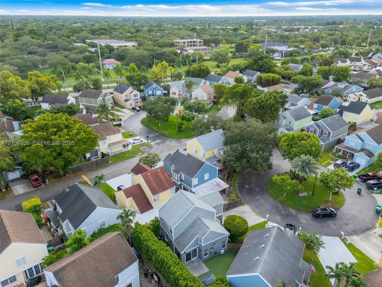 Aerial perspective of a residential neighborhood featuring paved streets, mature trees, manicured landscaping, and detached single-family dwellings with diverse rooflines