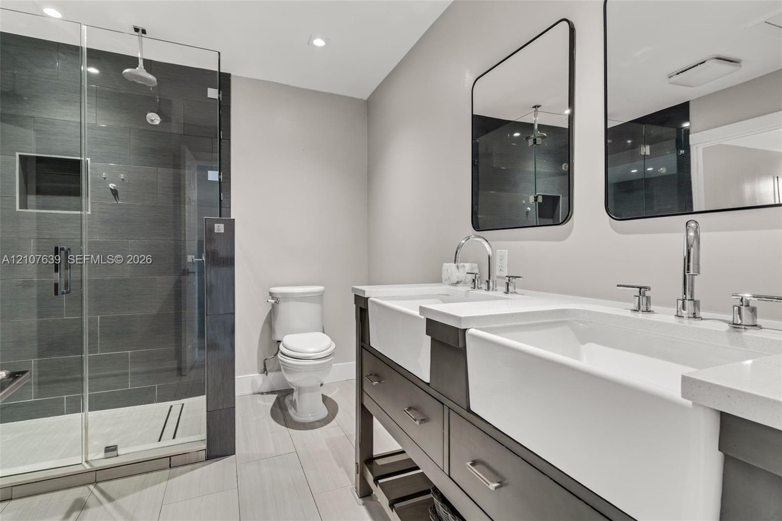 Double vanity featuring farmhouse-style sinks, quartz countertops, glass-enclosed shower with tiled walls, and dual rectangular wall-mounted mirrors
