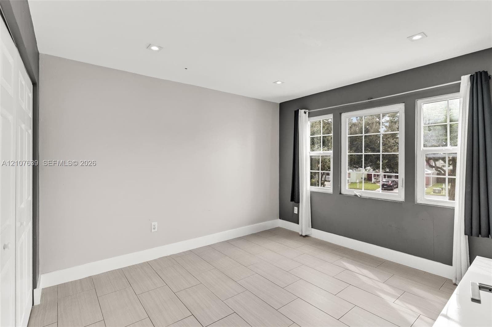 Neutral-toned room featuring large-format tile flooring, recessed ceiling lighting, three divided-light windows, and bi-fold closet doors