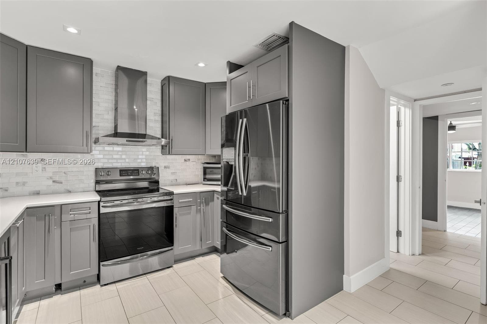 Kitchen featuring grey shaker-style cabinetry, white tile backsplash, stainless steel appliances, and large-format floor tile