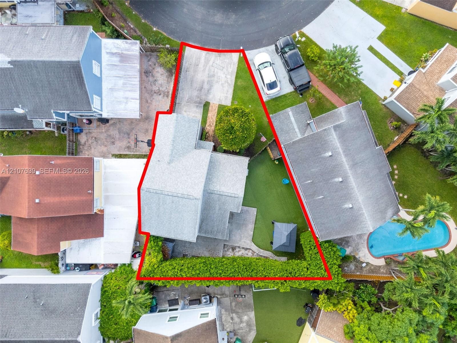 Cul-de-sac property featuring a concrete driveway, paved rear patio, and mature perimeter hedging