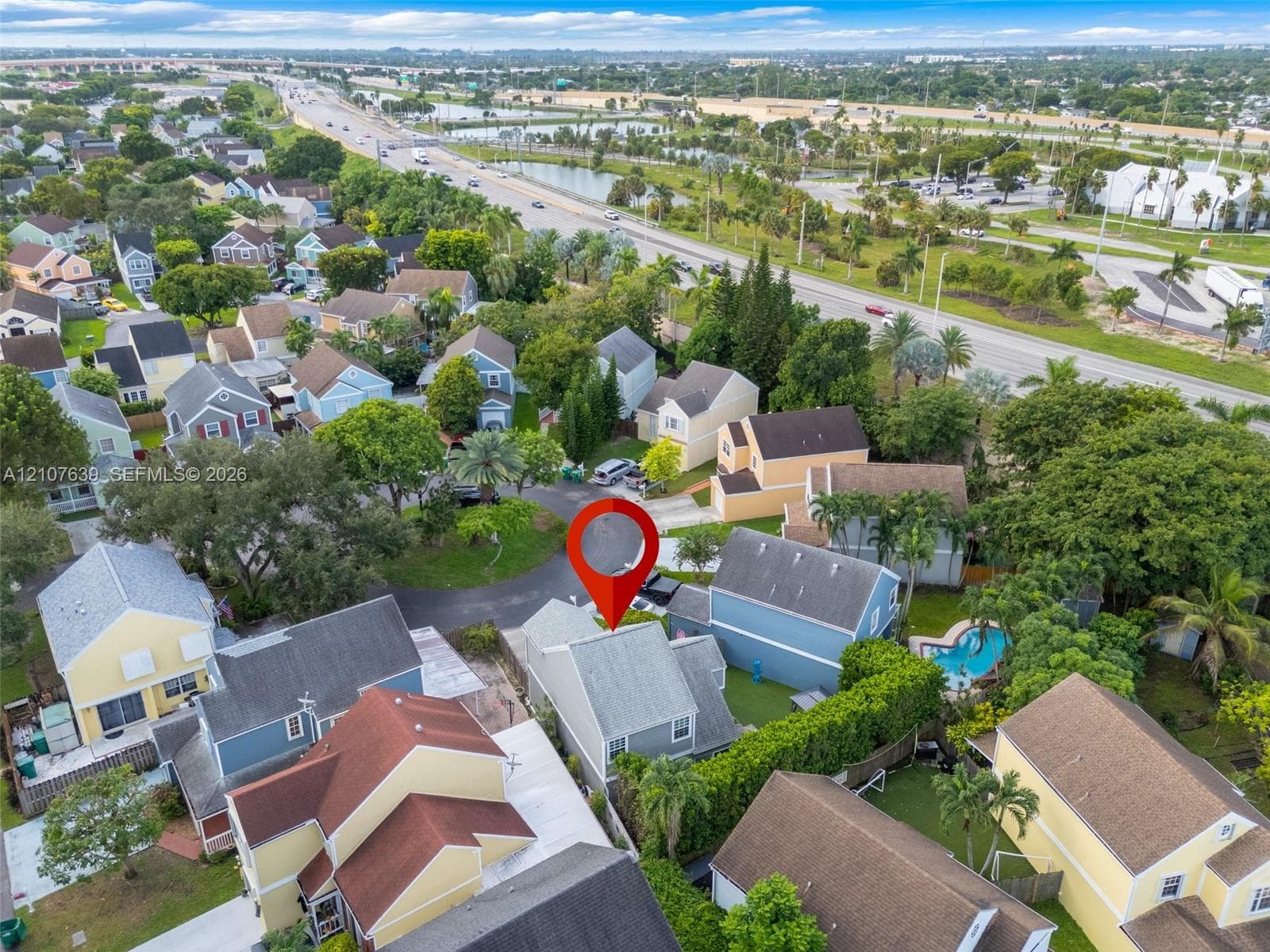 Aerial perspective of a multi-story residence featuring a shingled roof, asphalt driveway, and private swimming pool within a residential neighborhood