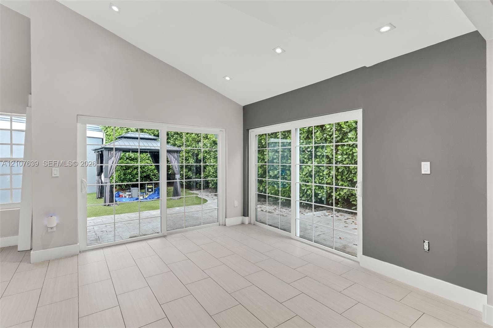 Vaulted ceilings, large-format tile flooring, dual sliding glass doors, and recessed lighting
