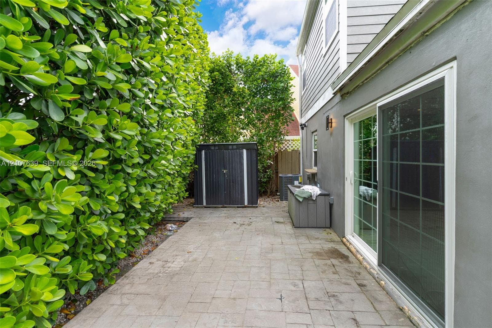 Side patio featuring paved hardscaping, a full-height privacy hedge, and sliding glass door entry