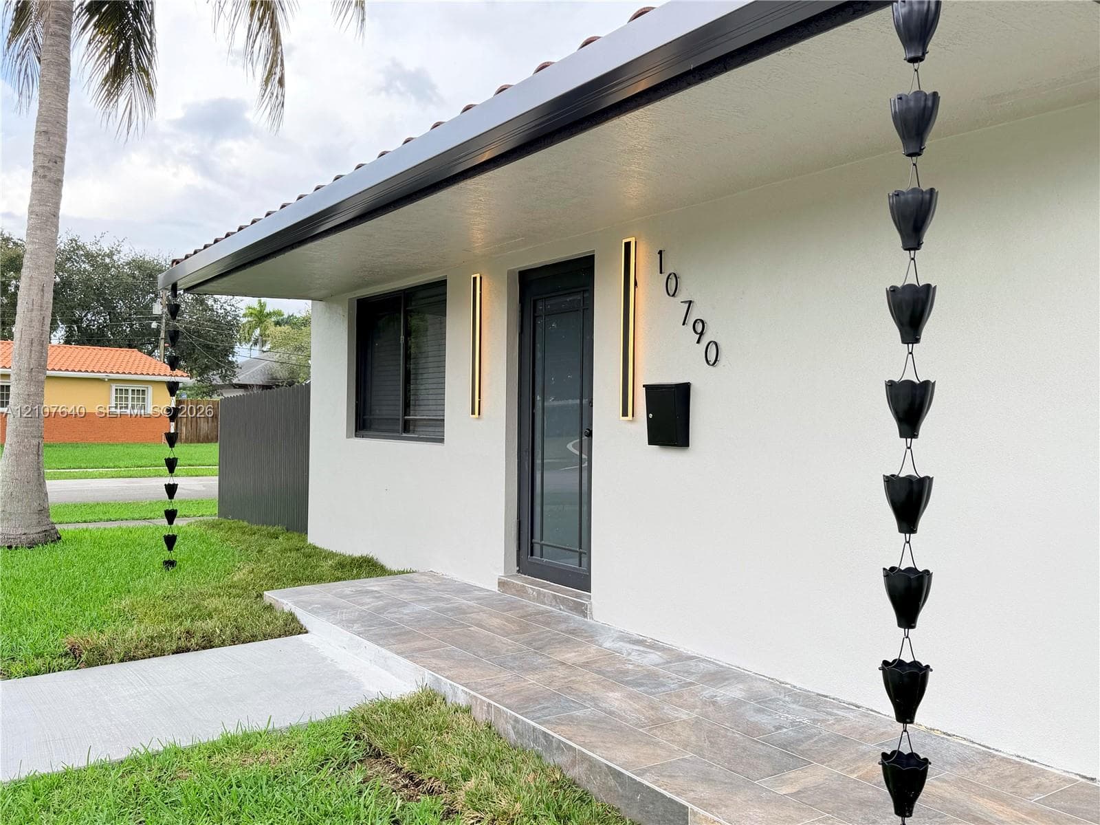 Exterior featuring a clean white facade, tiled porch entry, sleek vertical wall-mounted lighting, and matte black rain chains