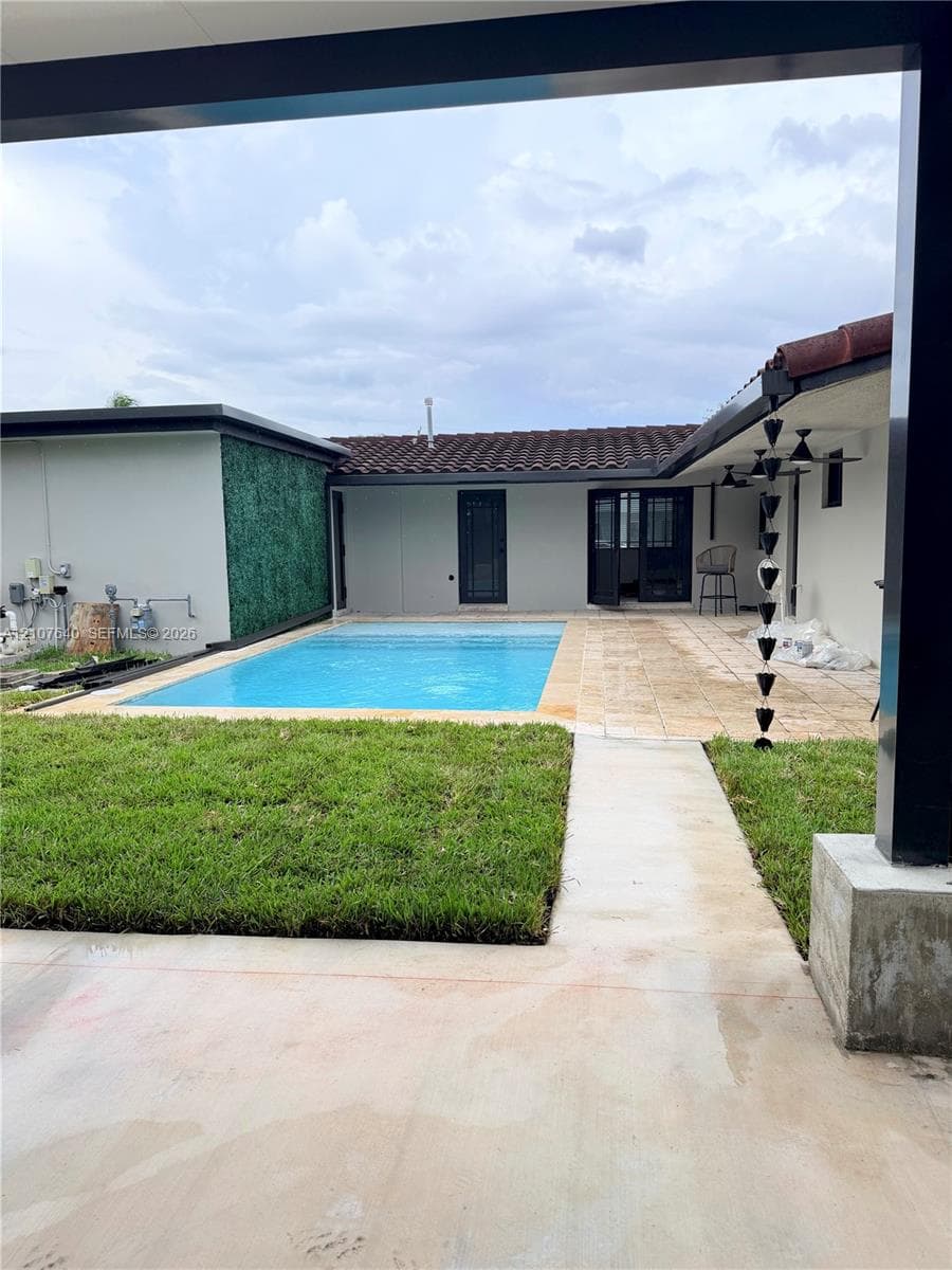 Private courtyard featuring an in-ground swimming pool, stone-paver patio, manicured lawn, and decorative green wall paneling