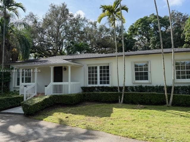 Single-story residence featuring a smooth stucco exterior, covered front porch with white railing, grid-pattern windows, and asphalt shingle roofing