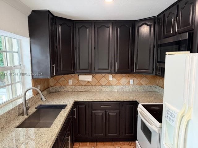 Kitchen featuring dark-finish cabinetry with silver-tone hardware, speckled stone-surface countertops, square tile backsplash, and stainless steel under-mount sink with gooseneck faucet