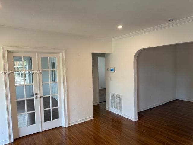 Interior space featuring wood-finish flooring, white French doors with glass panes, an arched architectural opening, and recessed ceiling lighting