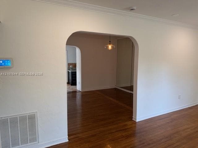 Arched doorways, wood-finish flooring, crown molding, a hanging pendant light fixture, and mirrored sliding closet doors