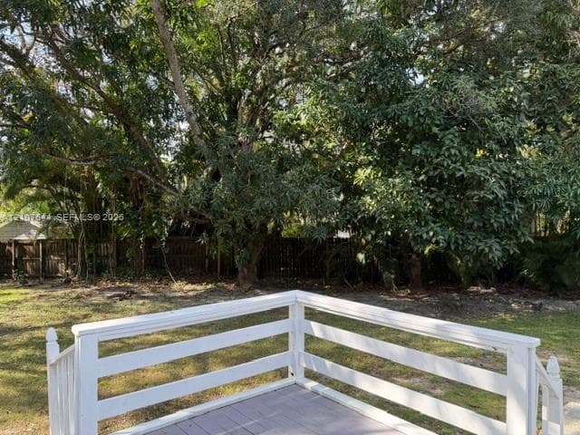 Raised wood deck featuring white horizontal-rail fencing and stairs, situated in a backyard with mature trees and perimeter wood fencing