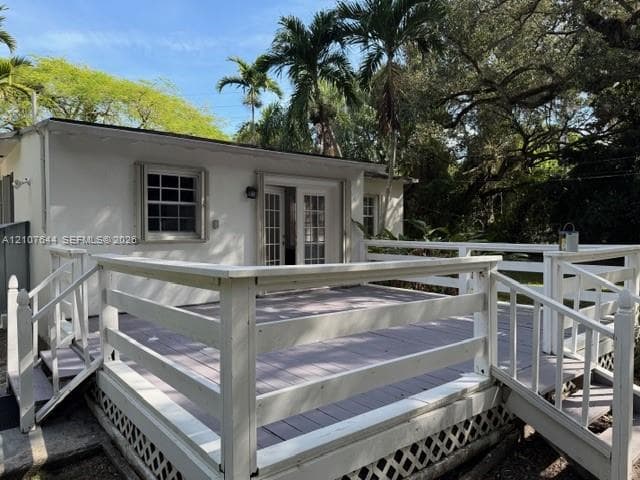 Exterior deck featuring white railings, dual staircases, and lattice skirting, finished with multi-pane French doors