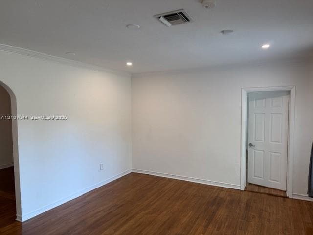 Neutral-toned interior space featuring wood-finish flooring, recessed lighting, crown molding, a decorative arched entryway, and a six-panel door