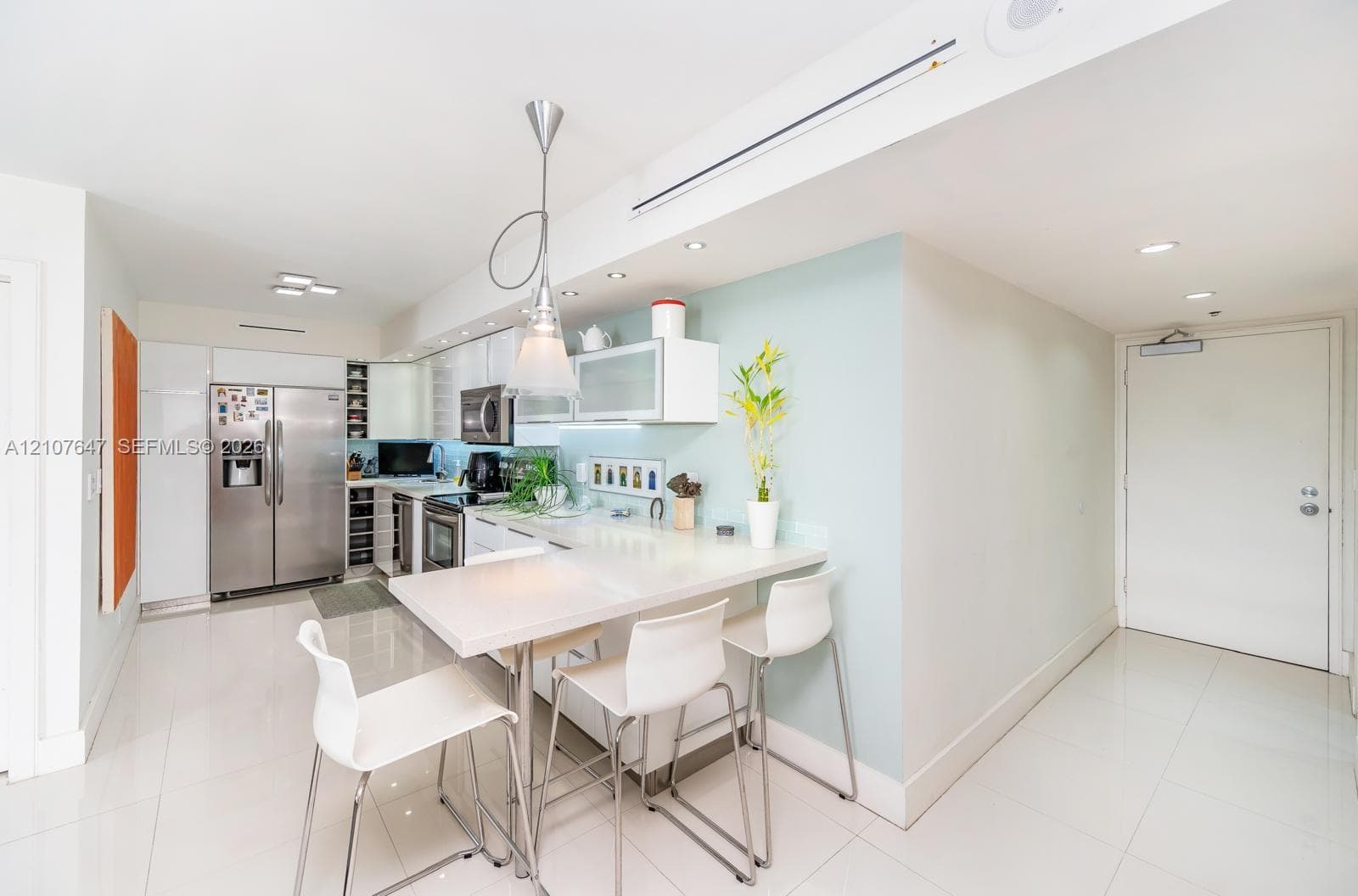 Kitchen featuring stainless steel appliances, white cabinetry, integrated breakfast bar with stone-surface countertop, polished tile flooring, and recessed ceiling lighting