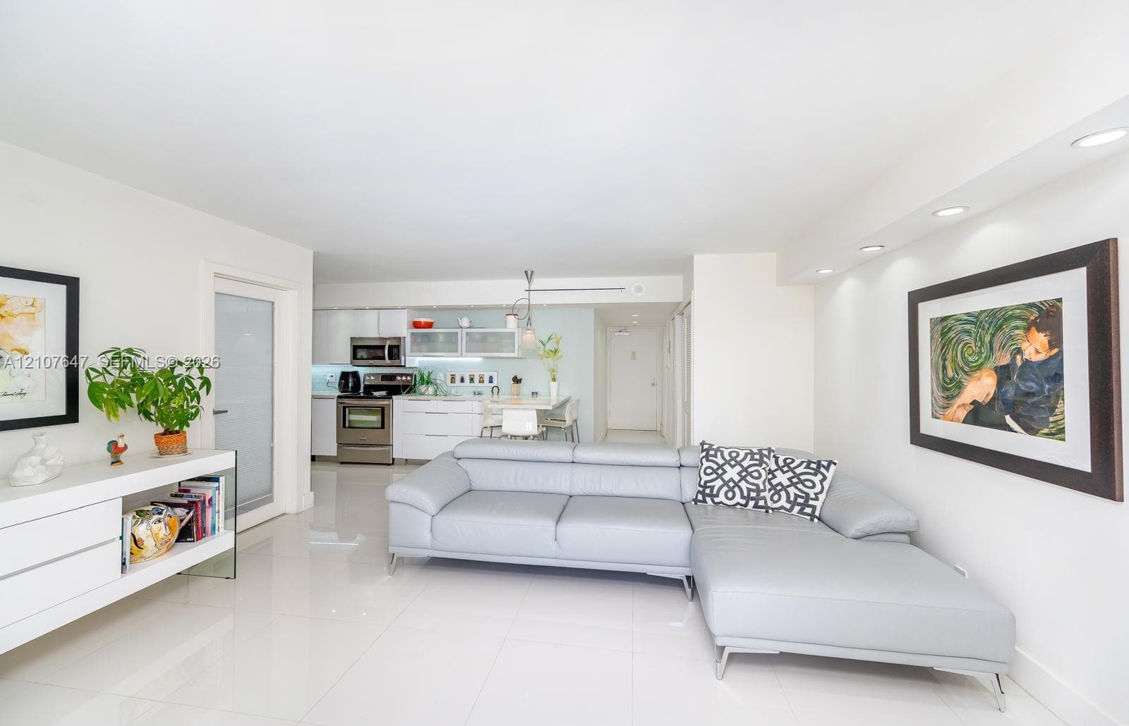 Open-concept living space featuring high-gloss white cabinetry, stainless steel appliances, recessed ceiling lighting, and polished tile flooring