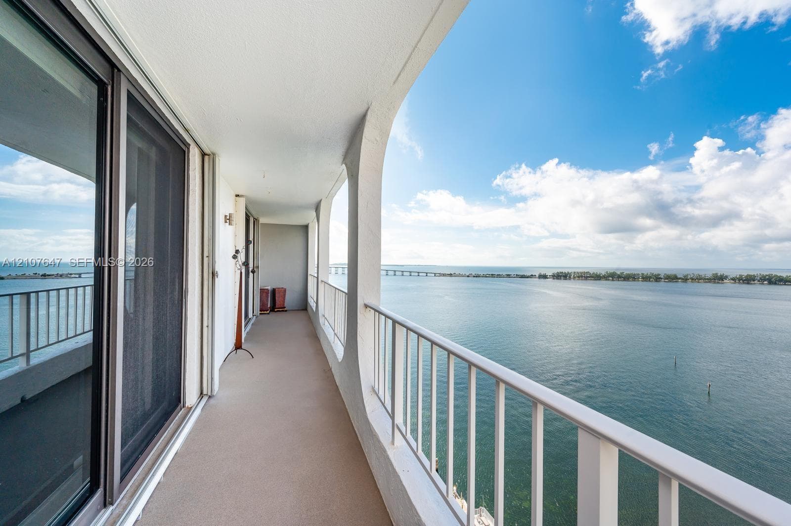 Covered balcony featuring concrete flooring, a white metal railing, and arch-style structural supports