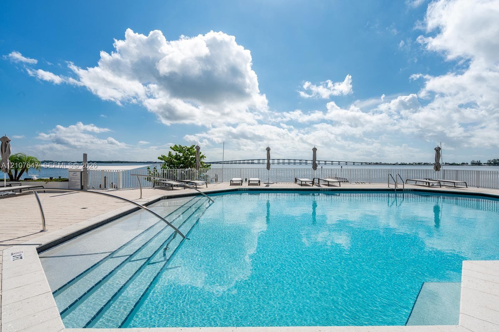 Swimming pool featuring a sun shelf entry, stainless steel handrails, tiled decking, and perimeter fencing
