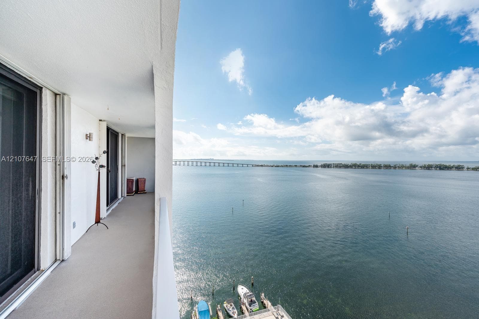 Covered exterior balcony featuring concrete flooring, sliding glass door access, and a metal railing