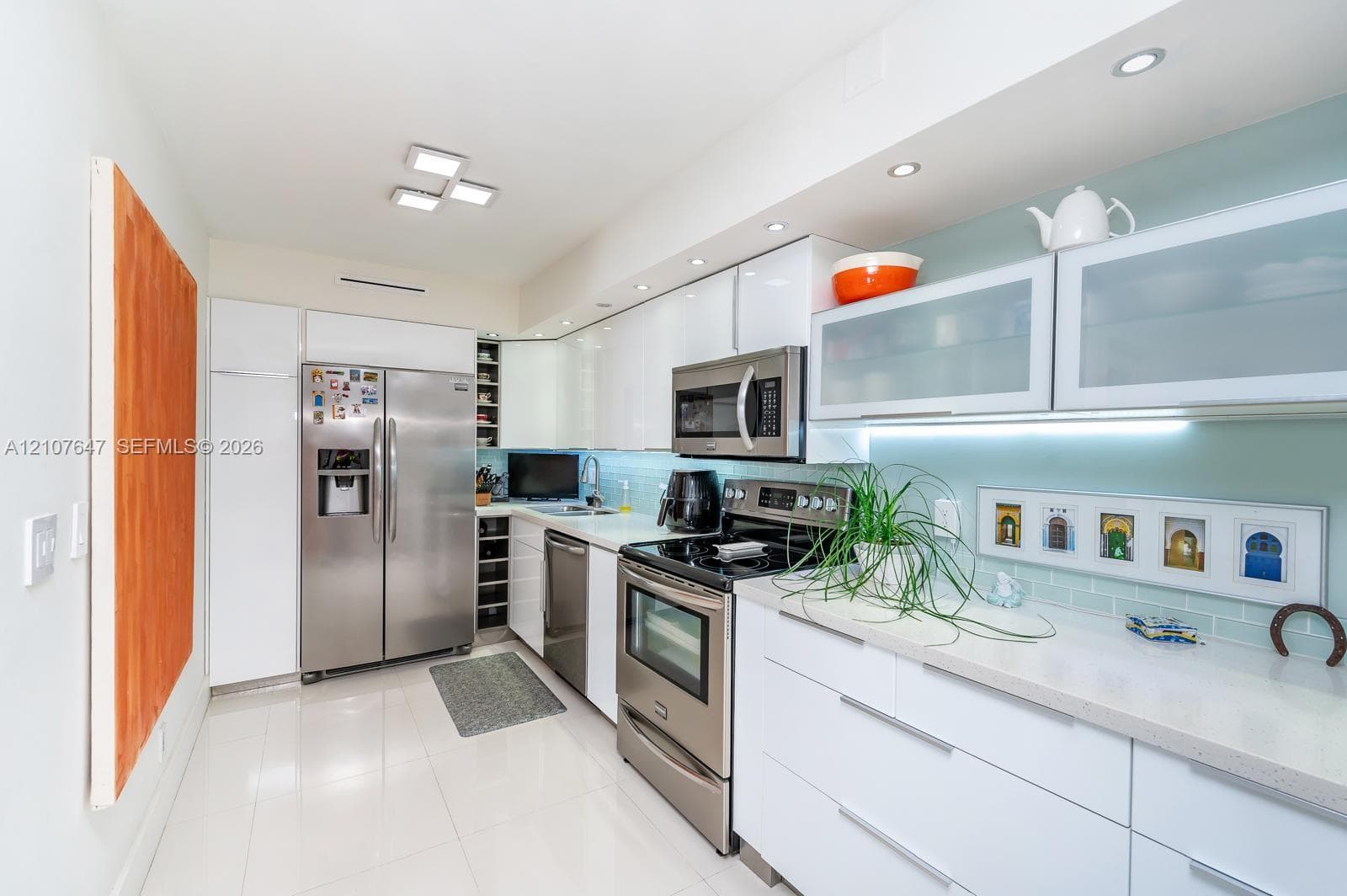 Kitchen featuring high-gloss white cabinetry, stainless steel appliances, light-toned stone countertops, glass-front upper cabinet doors, and recessed ceiling lighting