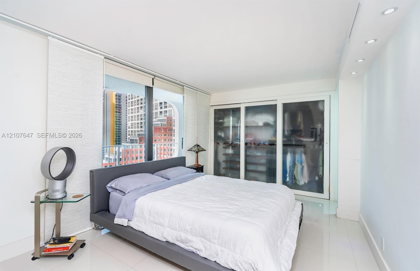 Floor-to-ceiling windows, built-in wardrobe with sliding frosted glass panels, recessed ceiling lighting, and polished stone-finish flooring