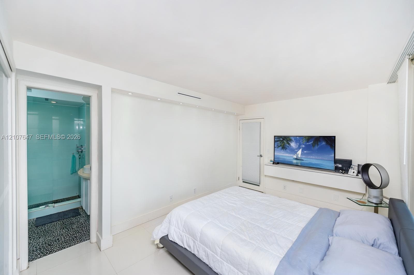 Recessed ceiling lighting, built-in wall-mounted media console, and a bathroom featuring a glass-enclosed shower with pebble-stone flooring