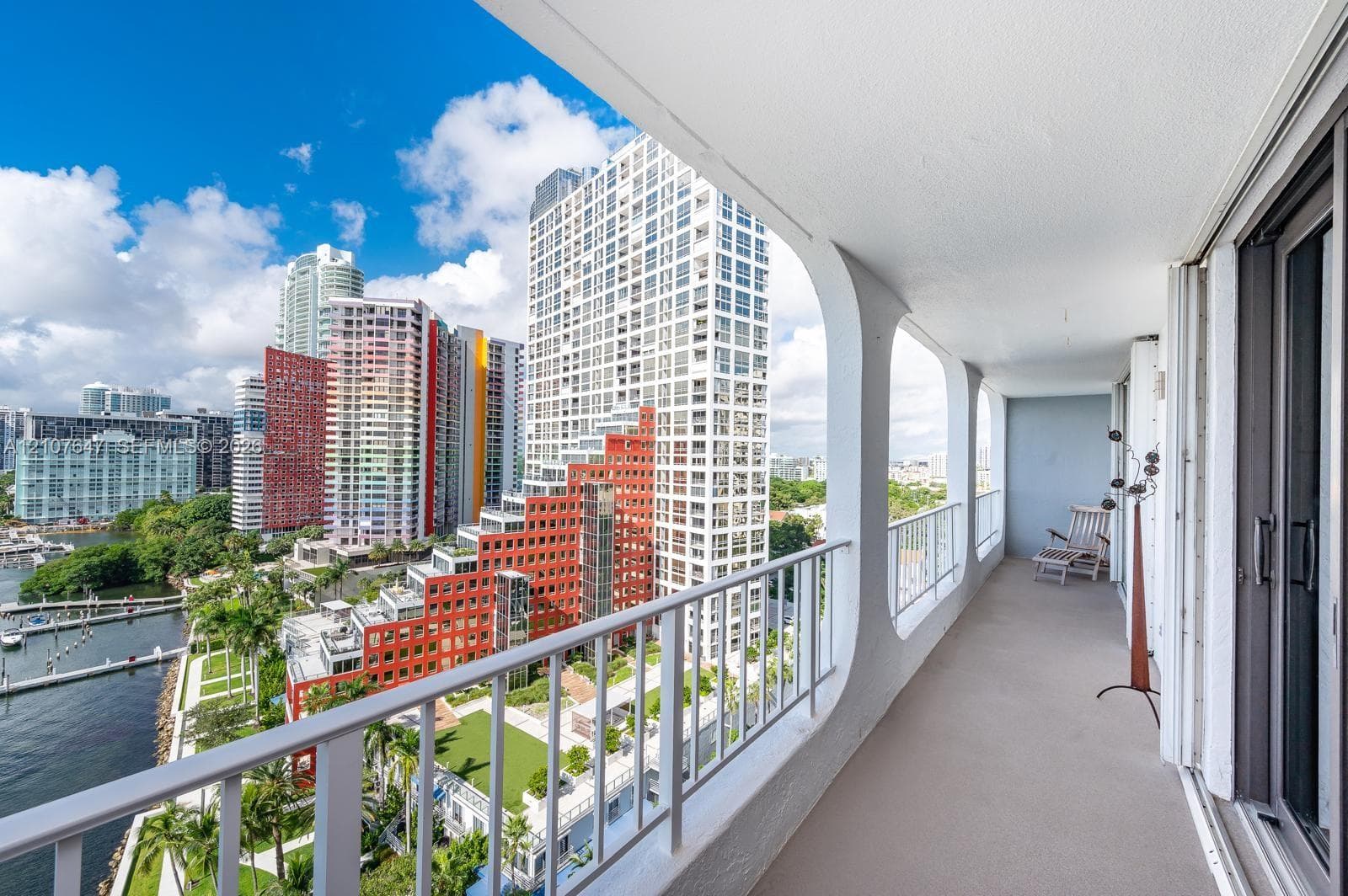 Covered balcony with white structural support pillars and metal railings overlooking an urban cityscape and waterfront
