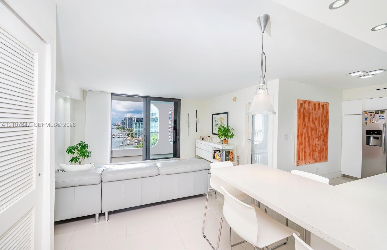 Open-concept area featuring light-toned tile flooring, recessed ceiling lighting, a neutral-toned kitchen island with stone-finish countertops, and floor-to-ceiling windows
