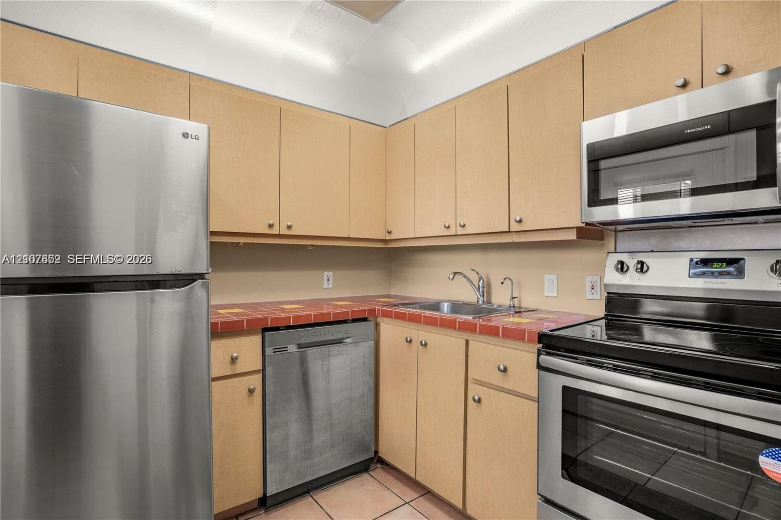 Kitchen featuring light-tone wood cabinetry, tiled countertops, stainless steel appliances, and tile flooring