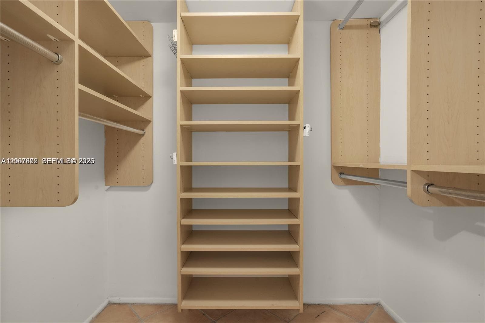 Walk-in closet featuring light wood-finish built-in shelving, vertical storage tower, dual metal garment rods, and tile flooring