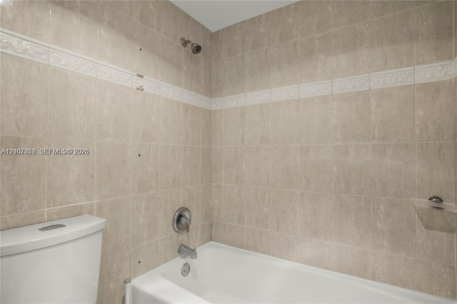 Bathtub and shower combination featuring neutral-toned wall tiles with a decorative accent border, a built-in recessed soap dish, and chrome-finish plumbing fixtures