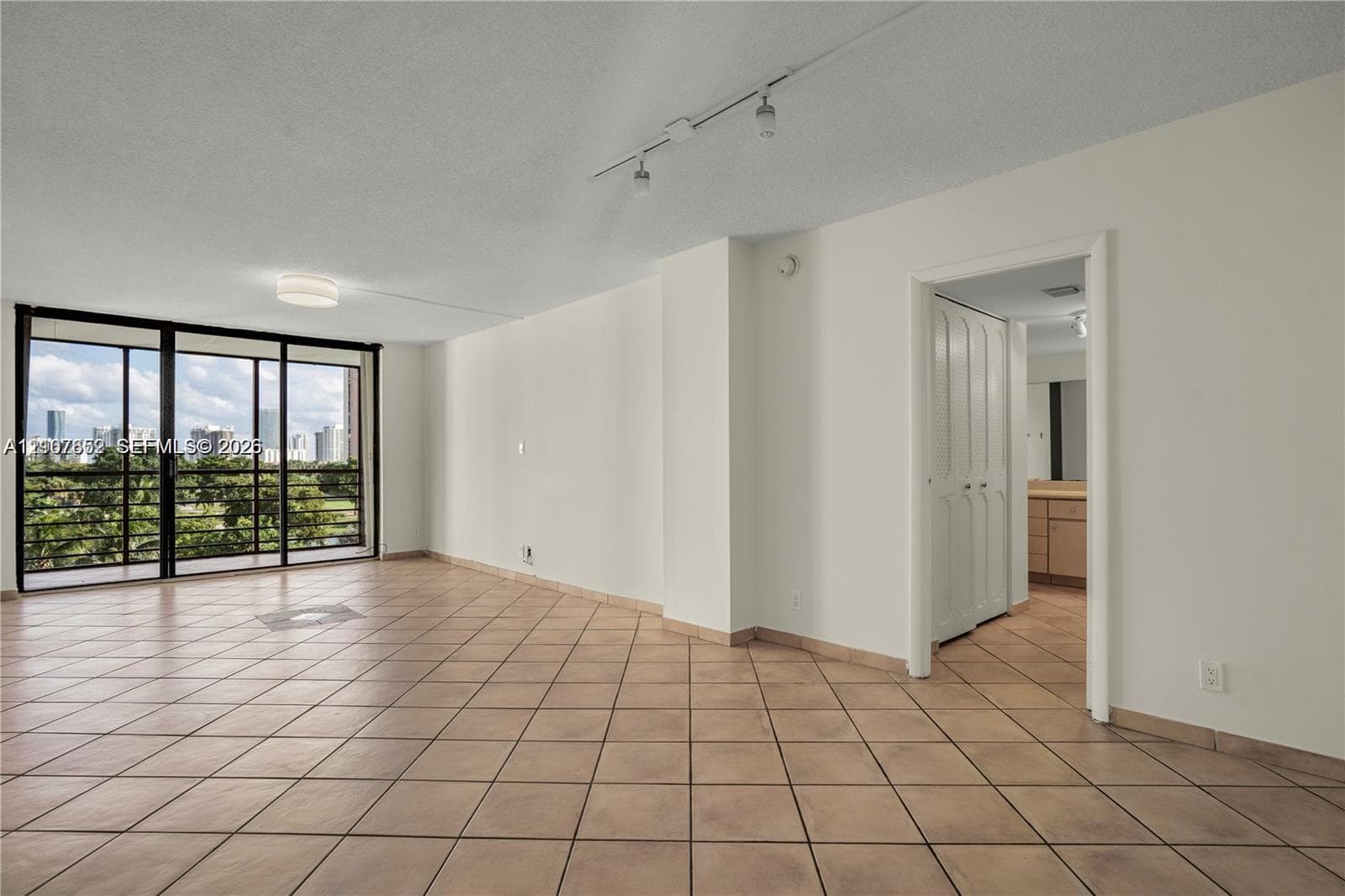 Open living space featuring neutral tile flooring, floor-to-ceiling sliding glass doors, adjustable track lighting, and built-in closet storage