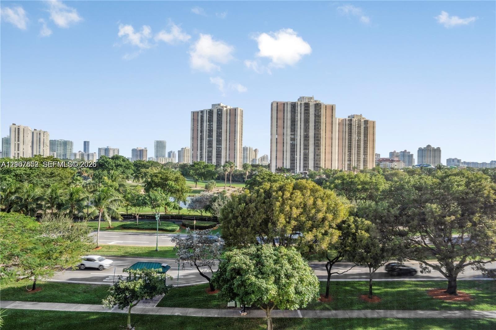 Panoramic urban skyline backdrop featuring expansive parkland, mature landscaping, and paved pedestrian pathways