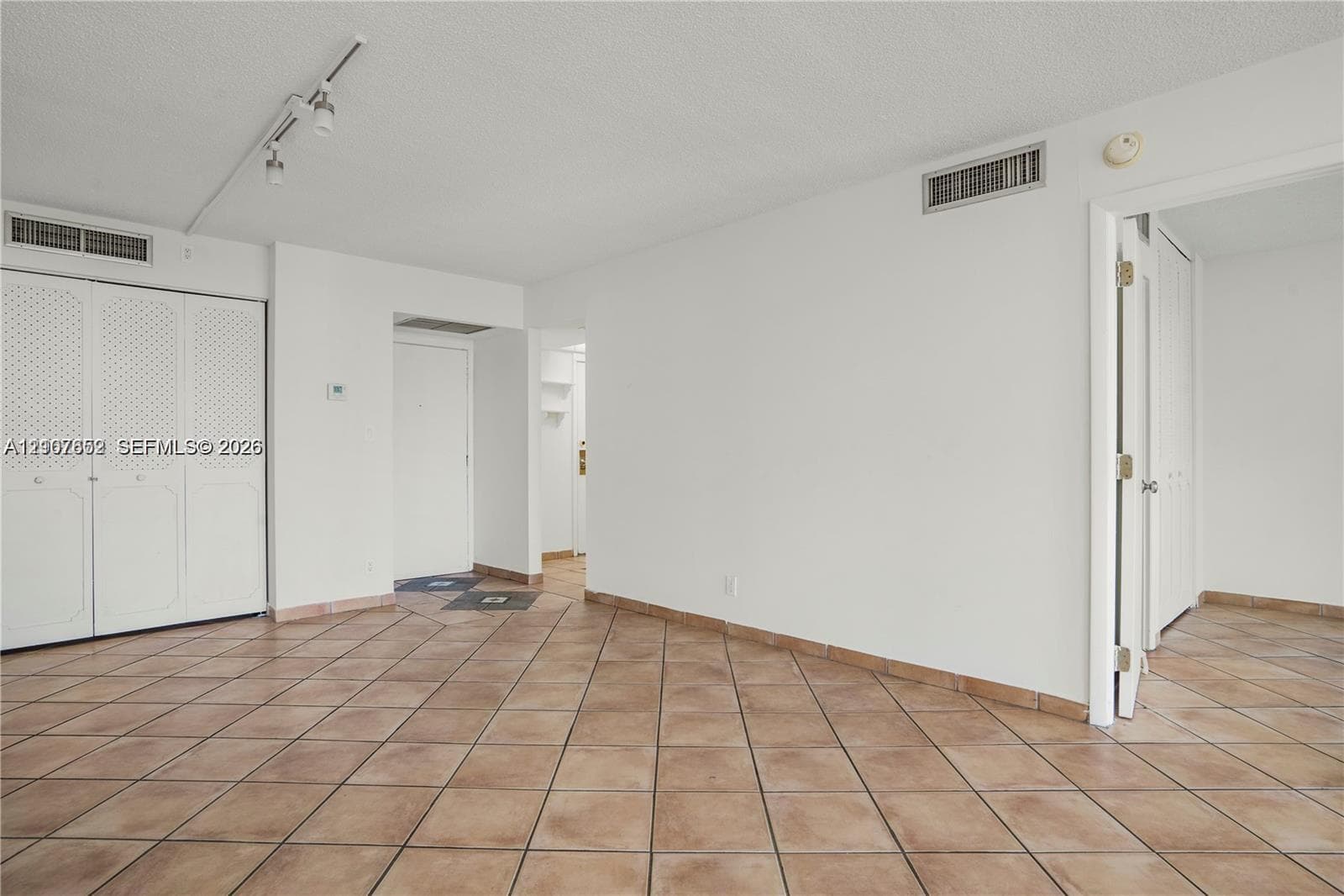 Open interior space featuring light-toned tile flooring, white bi-fold closet doors with decorative paneling, and adjustable track lighting