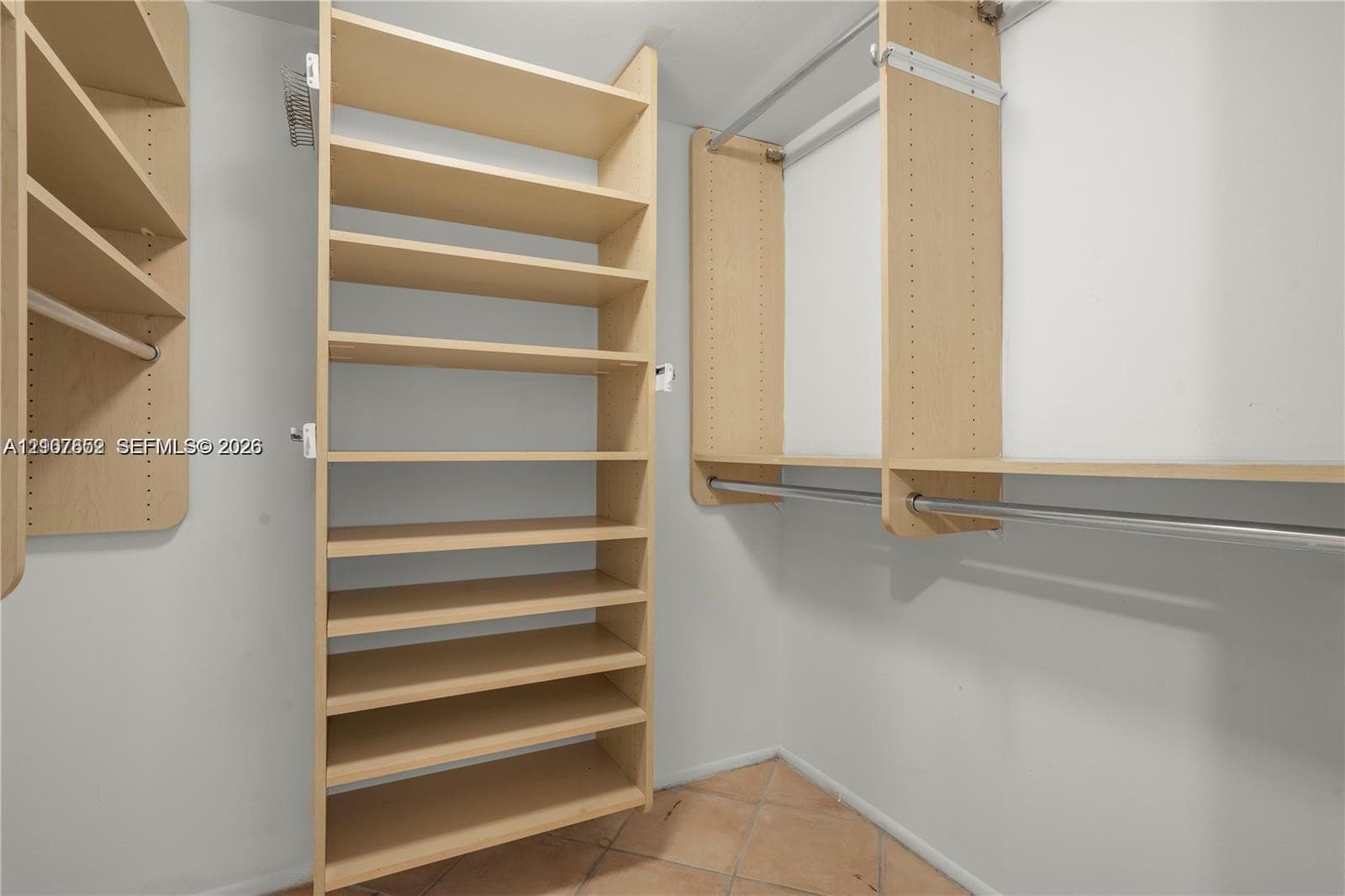 Custom walk-in closet featuring light-toned wood-finish shelving, multi-level hanging rods, and tile flooring