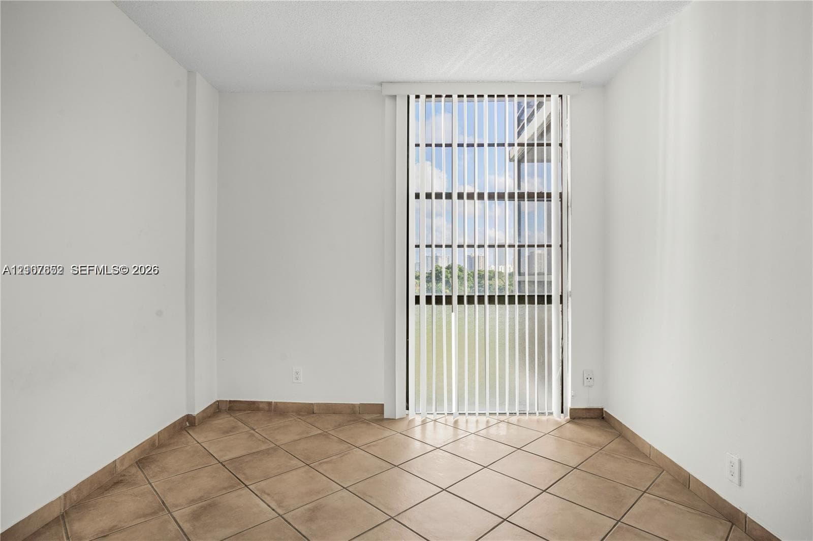 Room featuring neutral wall finishes, tile flooring, and a vertical blind covering a full-height glass door